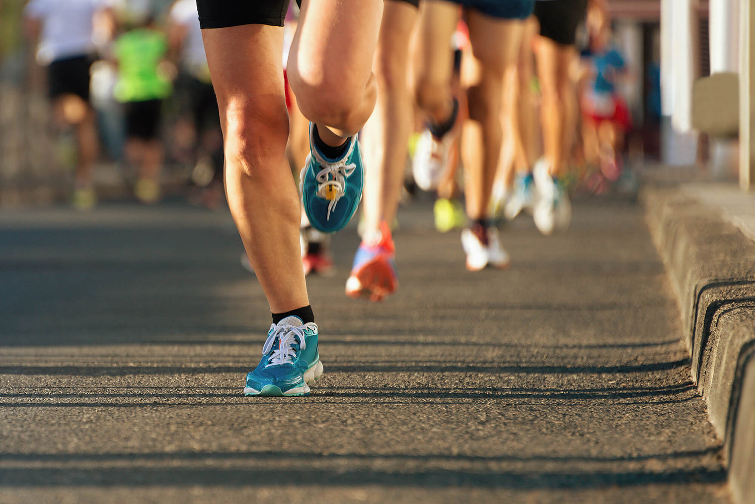 Vue au niveau du sol des jambes musclées de plusieurs coureurs en mouvement sur l’asphalte, lors d’une d’une course organisée de 15 km.