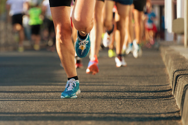 Vue au niveau du sol des jambes musclées de plusieurs coureurs en mouvement sur l’asphalte, lors d’une d’une course organisée de 15 km.